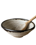 A beige ceramic bowl with a black rim, accompanied by a wooden spoon.