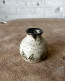 Small ceramic vase with black floral patterns on a sandy surface
