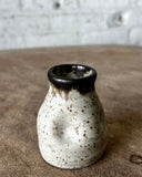 Speckled ceramic vase with black rim on a textured surface