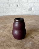 Small cherry red ceramic vase on a textured surface with a light gray background