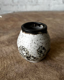 Ceramic tiny vase with black speckles and floral patterns on a textured surface