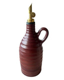 A dark red handmade olive oil bottle with a gold weighted pouring spout on a white background. 