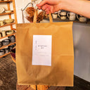 Brown tote bag with a label reading 'Mystery Box' held by a person in a pottery store.