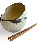 Stacked noodle bowls with chopsticks on a white background.