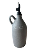 A gray handmade olive oil bottle with a black weighted pouring spout on a white background. 
