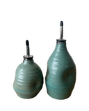 Two turquoise ceramic oil bottles with metal nozzles on a white background