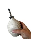 Hand holding a speckled ceramic bottle with a metal nozzle on a white background