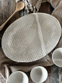 A caned ceramic print tray on a table with a table runner on a rustic wooden table. 
