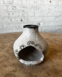Ceramic palo santo chiminea with black floral patterns on a wooden surface with a brick wall background