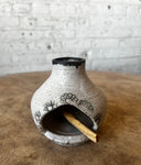 Ceramic chiminea with decorative patterns on a wooden surface and brick wall background