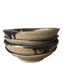 Stack of three ceramic bowls with black and beige speckled pattern on a white background