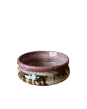 A pink, beige and bronze bowl with three thumbprints on a white background. 