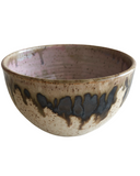 A handcrafted ceramic bowl with a speckled brown exterior and a pink interior with dark pink drips. The bowl also features beige, bronze, and white tones.