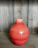 Red ceramic vase on a wooden surface with a wooden panel background