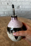 Hand holding a ceramic oil dispenser with a speckled design against a neutral background