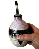 Hand holding a speckled ceramic oil bottle with a black cap on a white background
