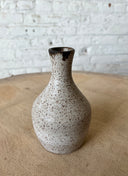 Speckled ceramic vase on a wooden surface with a white brick wall background