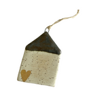 A ceramic house-shaped ornament with a bronze roof and white body, hanging from a twine.