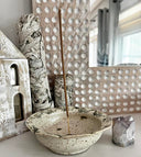 Ceramic bowl with incense stick, decorative stones, and crystal on a light surface.