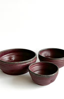 Three ceramic bowls with a maroon and black glaze on a white background
