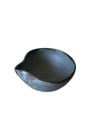 A hand holding a small, beige and brown ceramic pouring bowl with a spout.