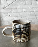 Ceramic mug with black and white speckled pattern on a concrete surface with a light gray brick wall background.