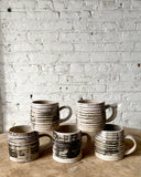 Set of ceramic mugs with striped design on a wooden surface against a white brick wall.
