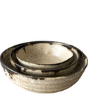 A set of three beige ceramic nesting bowls with rustic finishes and organic shapes, stacked together.