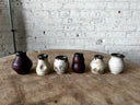 Set of six ceramic vases on a wooden table with a brick wall background