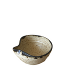 A hand holding a small, beige and brown ceramic pouring bowl with a spout.