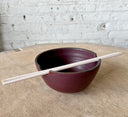 A beige and brown stoneware noodle bowl with a satin matte finish and bronze accent at the lip, accompanied by a pair of chopsticks resting on the bowl.