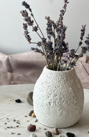 White textured vase with dried lavender on a light wooden surface.