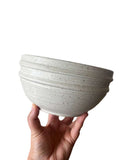 Beige bowl on a white background being held by a hand. 