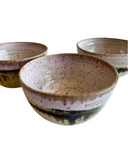 Three ceramic bowls with speckled glaze on a white background
