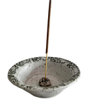 Ceramic incense holder with speckled design and a single incense stick on a white background