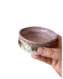 A pink, beige and bronze bowl with three thumbprints  being held by a hand on a white background. 