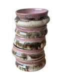 A stack of  pink, beige and bronze bowl with three thumbprints on a white background. 