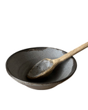 A beige ceramic bowl with a black rim, accompanied by a wooden spoon.