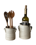 Ceramic utensil holder with wooden spoons and a wine bottle in a ceramic cooler on a white background