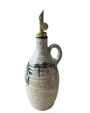 A beige and bronze handmade olive oil bottle with a gold weighted pouring spout on a white background. 