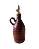 A dark red handmade olive oil bottle with a gold weighted pouring spout on a white background. 