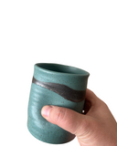 Hand holding a teal ceramic mug with a dark brown accent on a white background