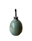 Teal ceramic oil dispenser with a black cap on a white background
