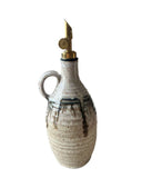 A beige and bronze handmade olive oil bottle with a gold weighted pouring spout on a white background. 