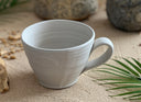 Two ceramic mugs, one with a smoother exterior and the other with a textured exterior, both in a off white color.