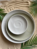 White and green plates sit atop sand and fern leaves. 