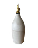 A white ceramic oil pourer with a weight gold pouring spout on a white background. 